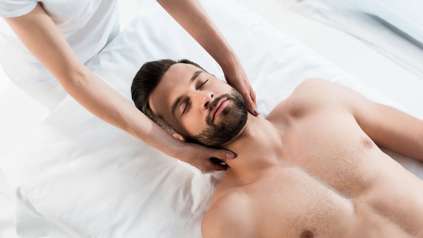 cropped view of masseur doing neck massage to handsome man with closed eyes