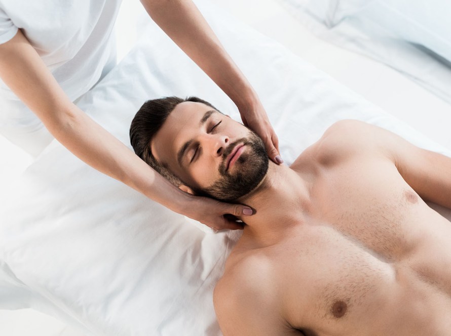 cropped view of masseur doing neck massage to handsome man with closed eyes
