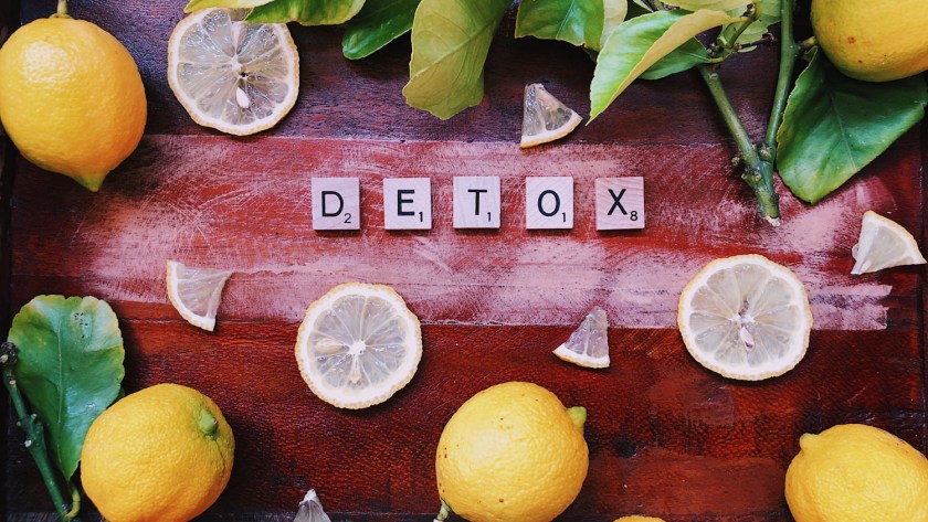 lemons slices & wedges on a wooden table with lemon leaves & letters spelling "detox."