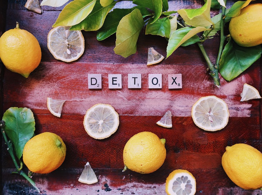 lemons slices & wedges on a wooden table with lemon leaves & letters spelling "detox."