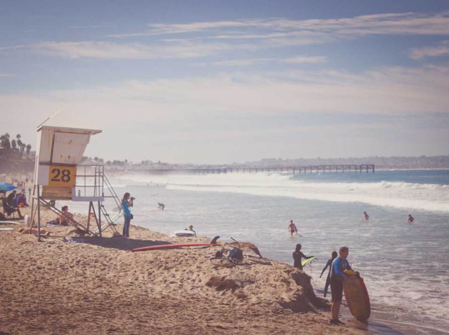 A picturesque view of Pacific Beach, a lifeguard station, surfers and beach enthusiasts enjoying the scenery.