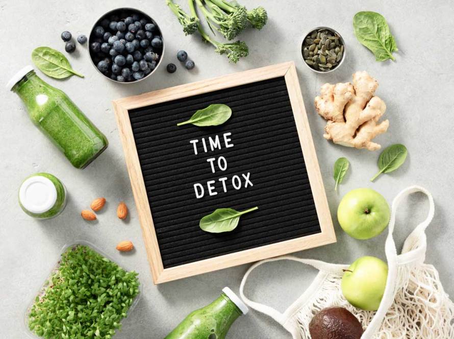 A cornucopia of fruit, vegetables, herbs, nuts, & juices with a sign reading Time to Detox, with basil leaves framing the words.