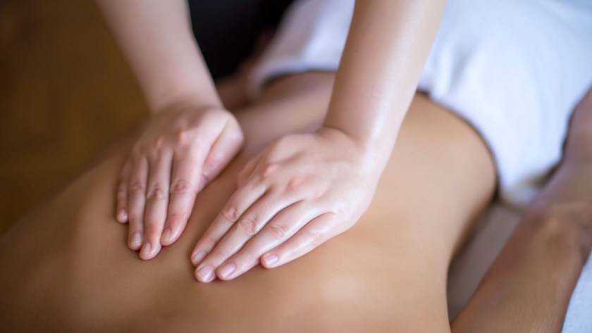 Massage therapists oily hands rubbing an athletic back to soothe & work out tension.