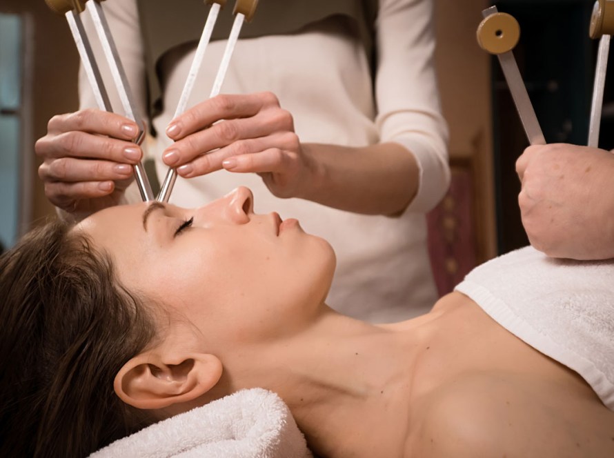 Woman receiving sound healing therapy using tuning forks while she rests & recovers.